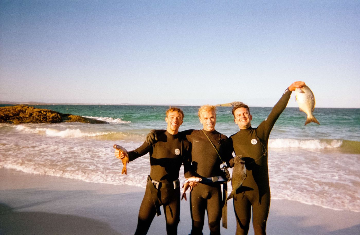 Three men in wetsuits holding up the fish they speared