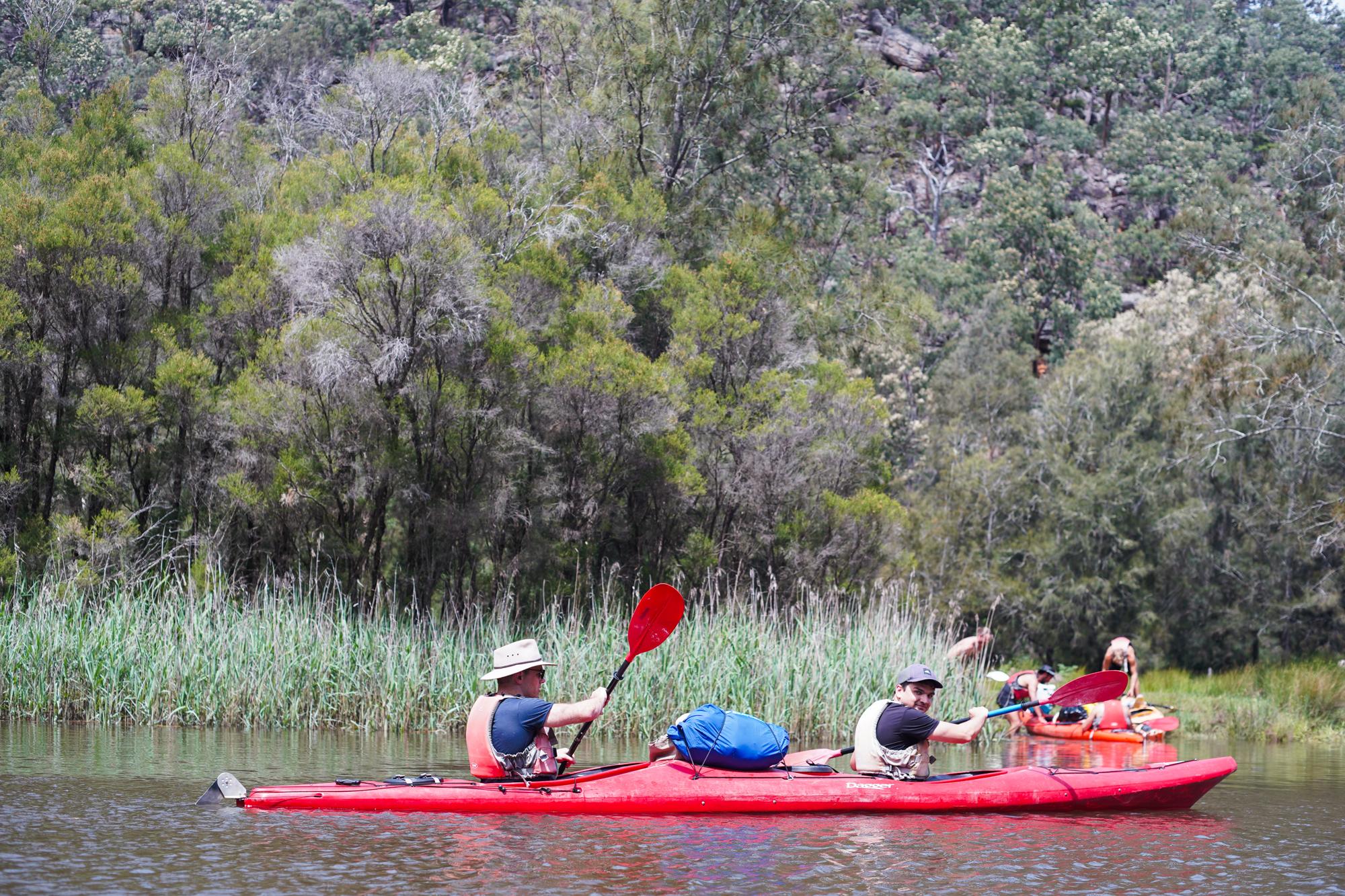 Men paddling past reeds on a bush river