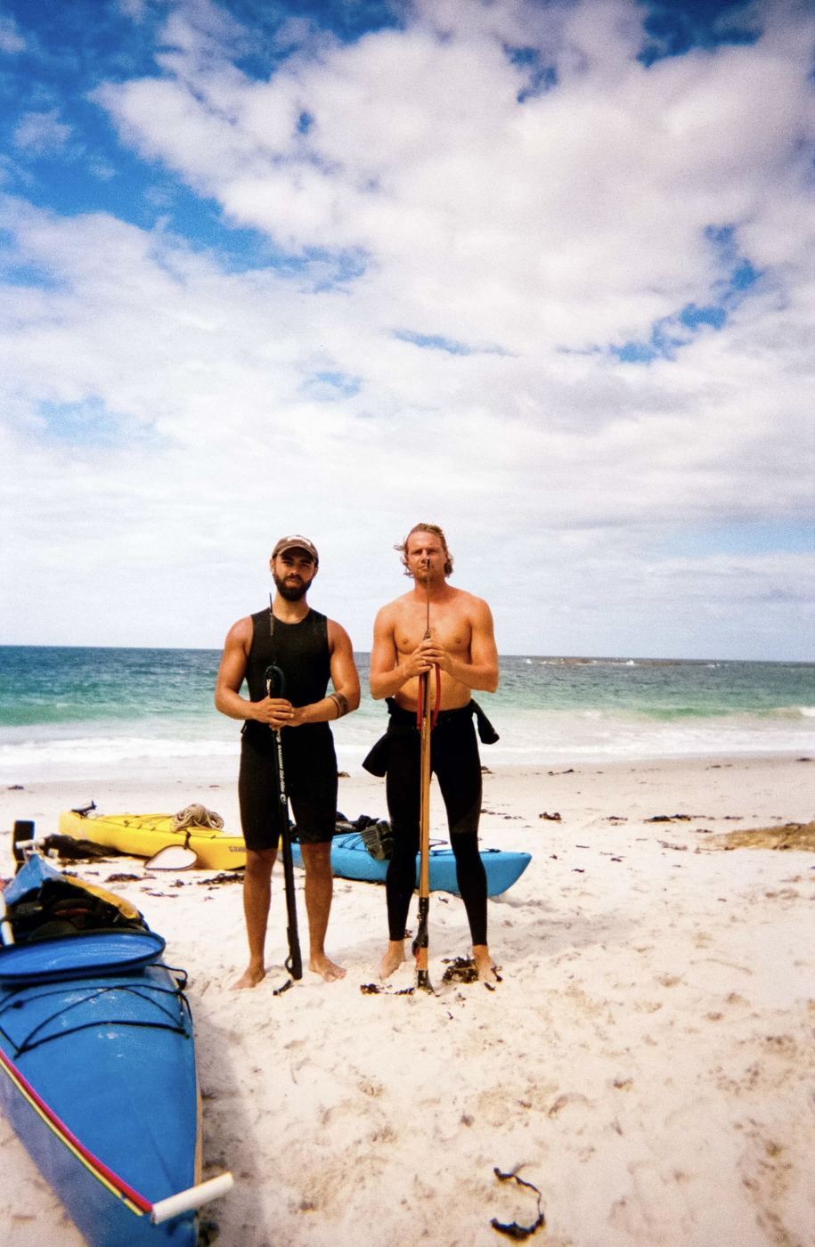 Two men in wetsuits with spearguns beside the kayaks