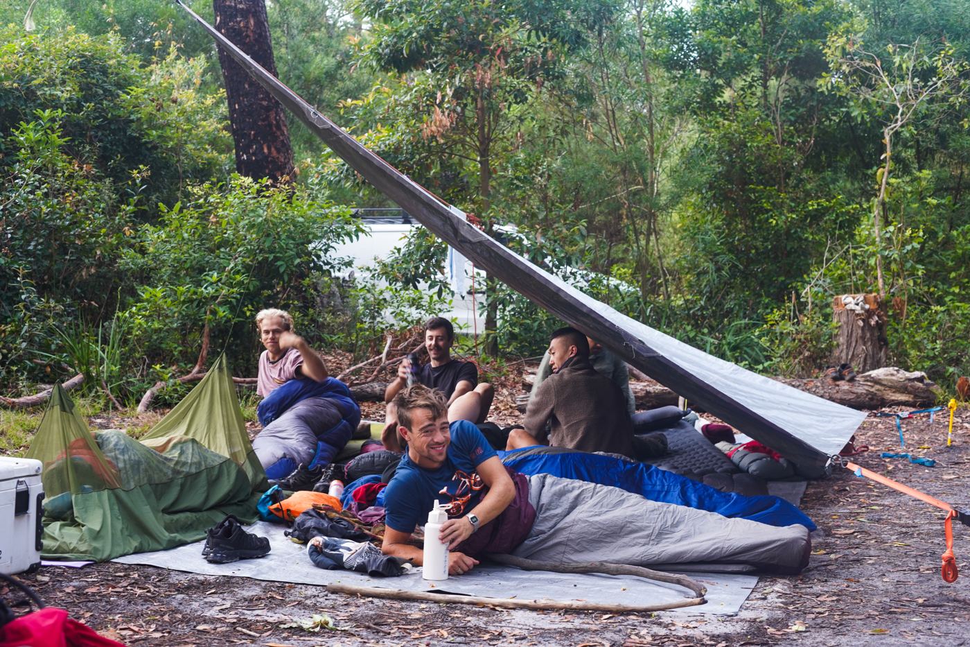 Men in sleeping bags under a tarp in the bush