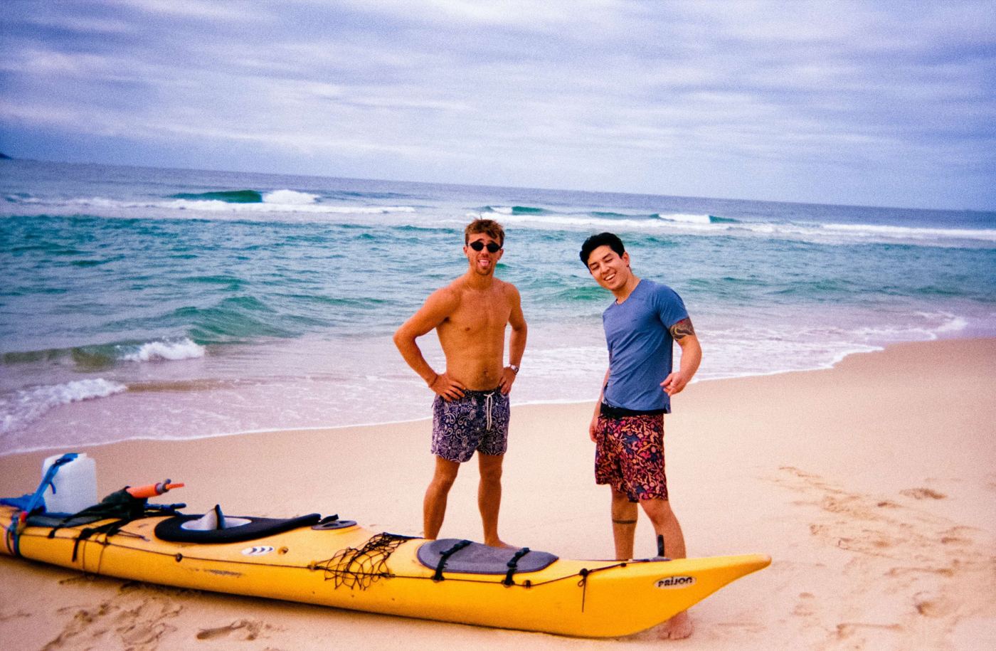 Two men standing by a yellow sea kayak on the beach