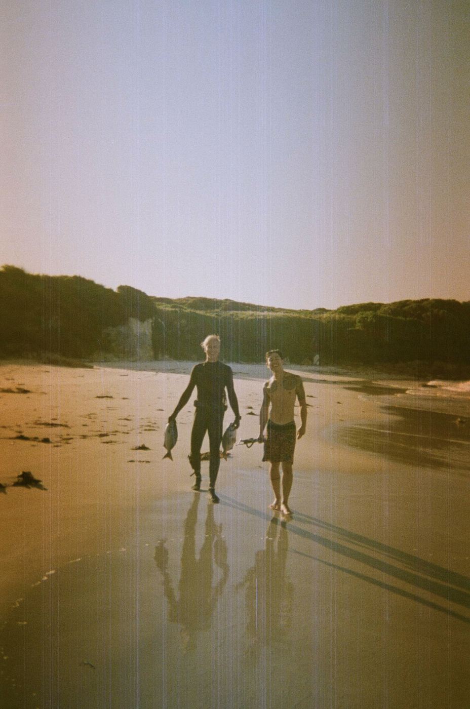 Two men walking along the beach carrying fish